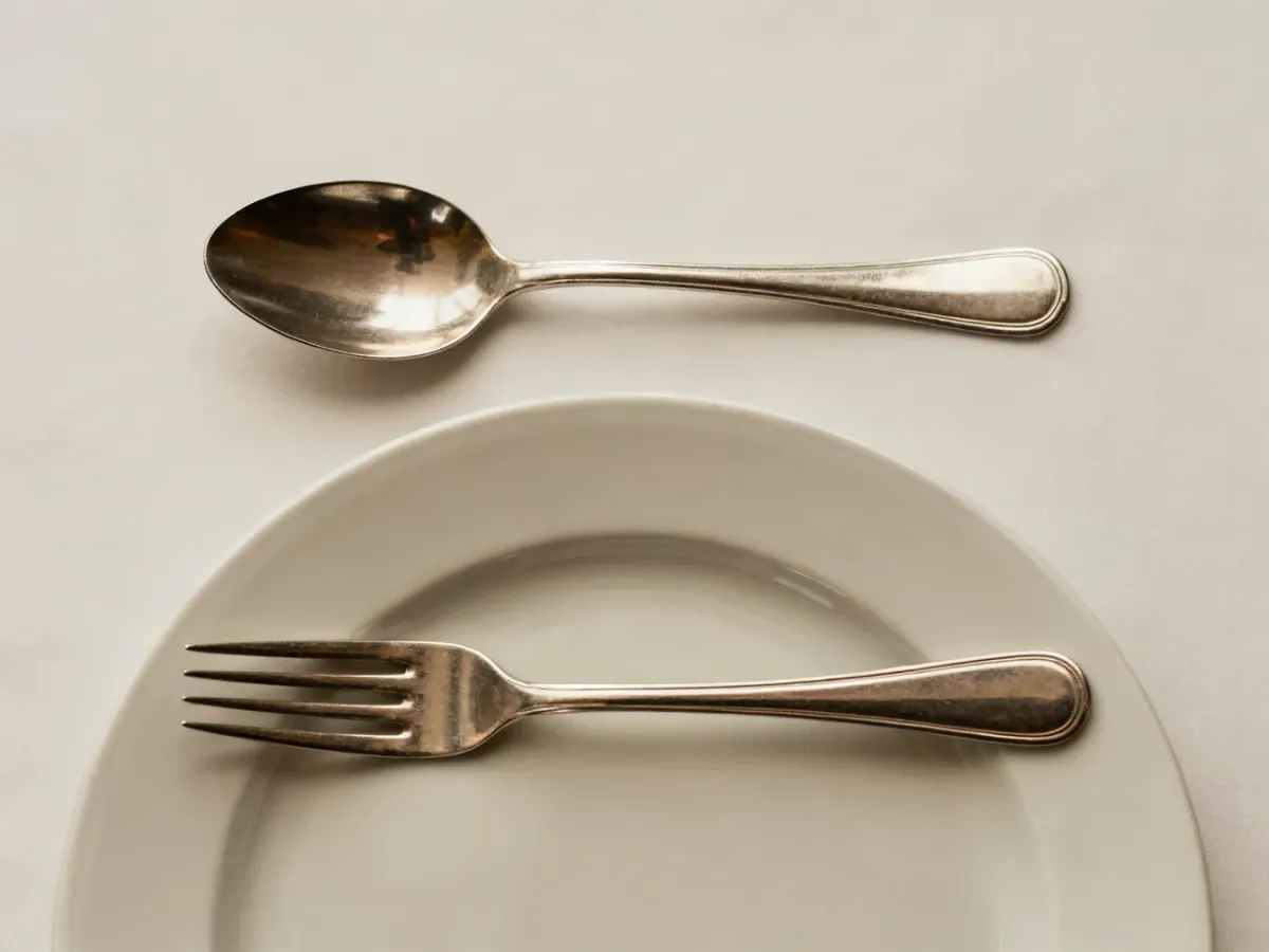 Dessert spoon and fork arranged horizontally above a dinner plate